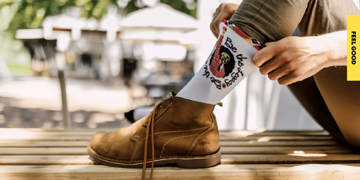 Nelson Mandela Day Custom Socks Donation A close-up of a custom sock featuring the Nelson Mandela Day campaign logo being pulled up, worn with a leather shoe to celebrate our community support initiatives.
