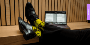 Legs resting on a table showing professional office attire contrasted with vibrant custom socks, illustrating how socks can serve as a unique business card.